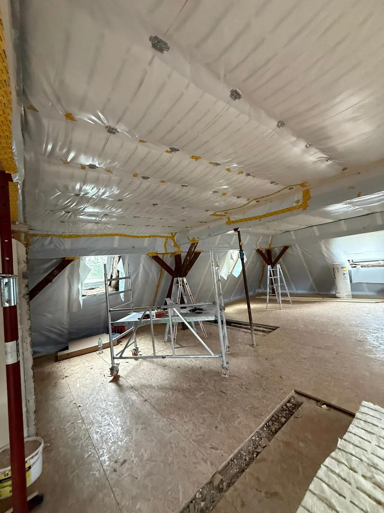 Augsburg, Hauptfläche des Dachgeschosses vor dem Ausbau: offener Rohdachboden mit Dampfbremsfolie, Baustützen und provisorischem Holzboden