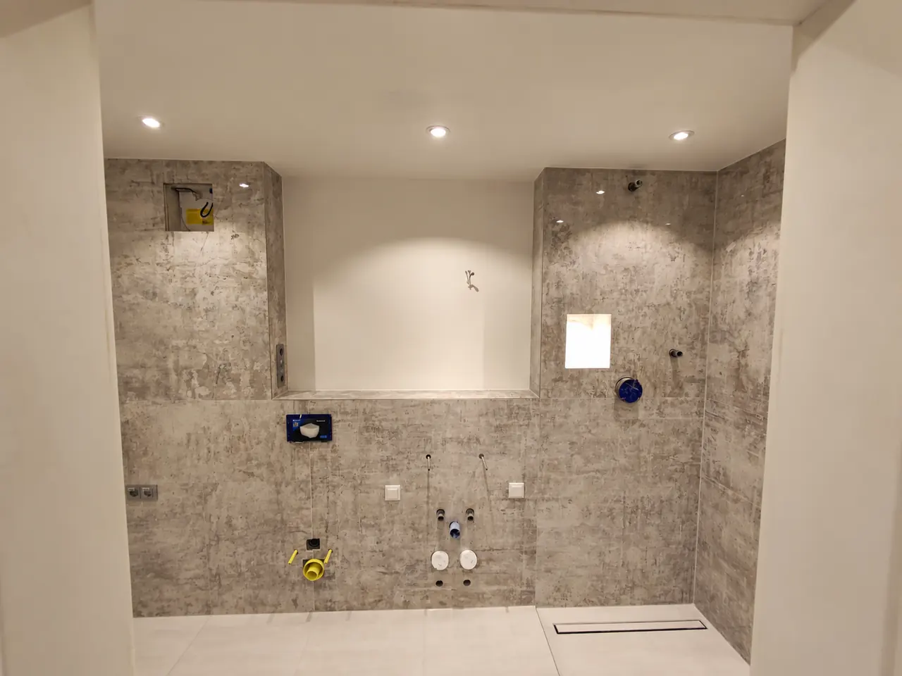 Badezimmer im Baufortschritt: geflieste Wände in Betonoptik mit vorbereiteten Anschlüssen