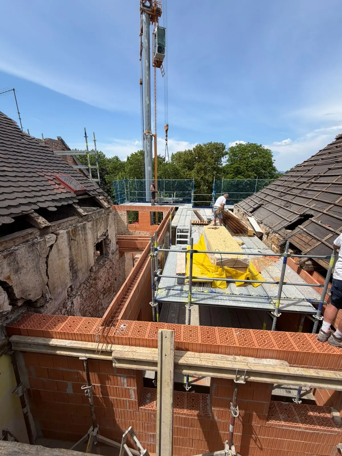 Dachboden-Ausbau: neues Ziegelmauerwerk zwischen geöffneten Dachflächen, im Hintergrund ein Baukran