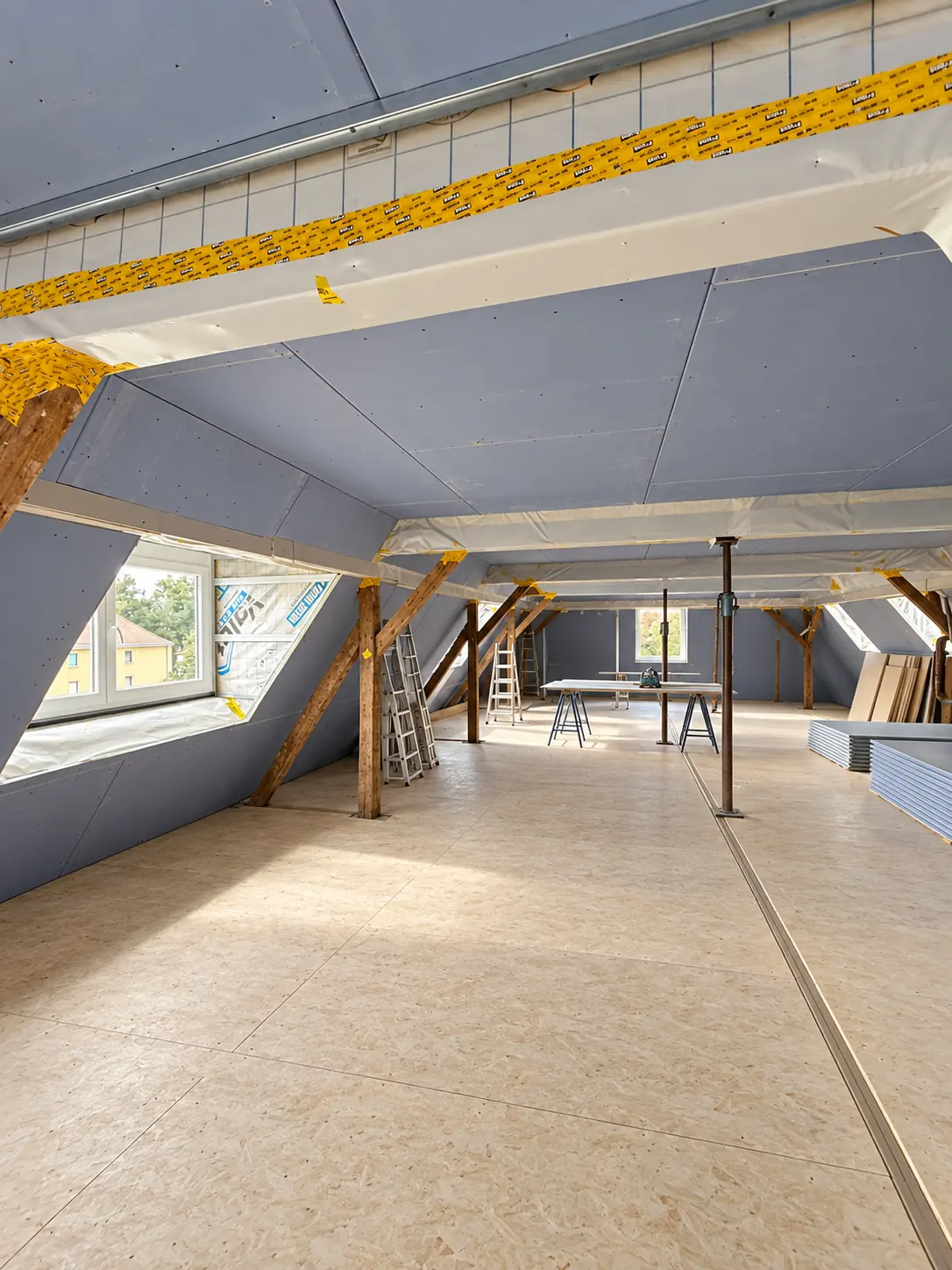 Dachgeschoss im Ausbau: offener Raum mit Holzbalken, Dachfenstern und frisch verlegtem Estrich