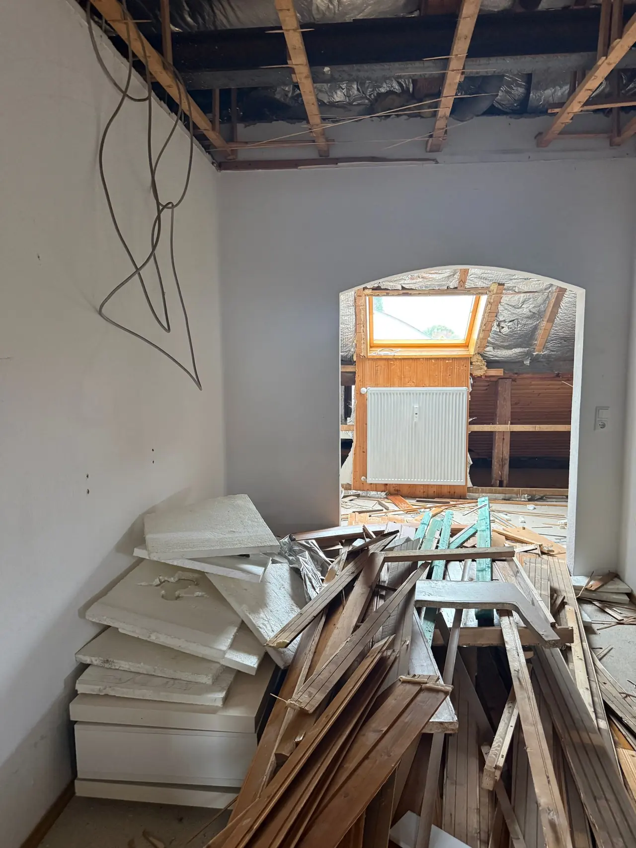 Abbruch im Bestand: geöffnete Decke mit freiliegenden Kabeln, davor Haufen aus Abbruchholz