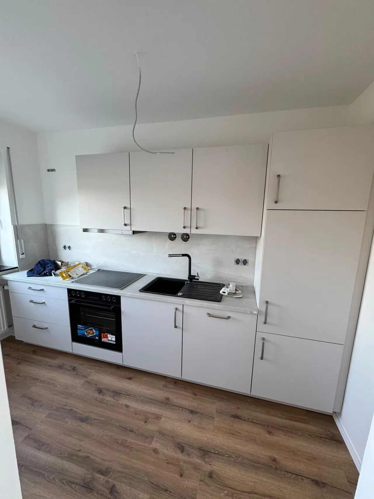 Straubing, Küche nach der Sanierung: weiße Einbauküche mit Kochfeld, Backofen und Spüle
