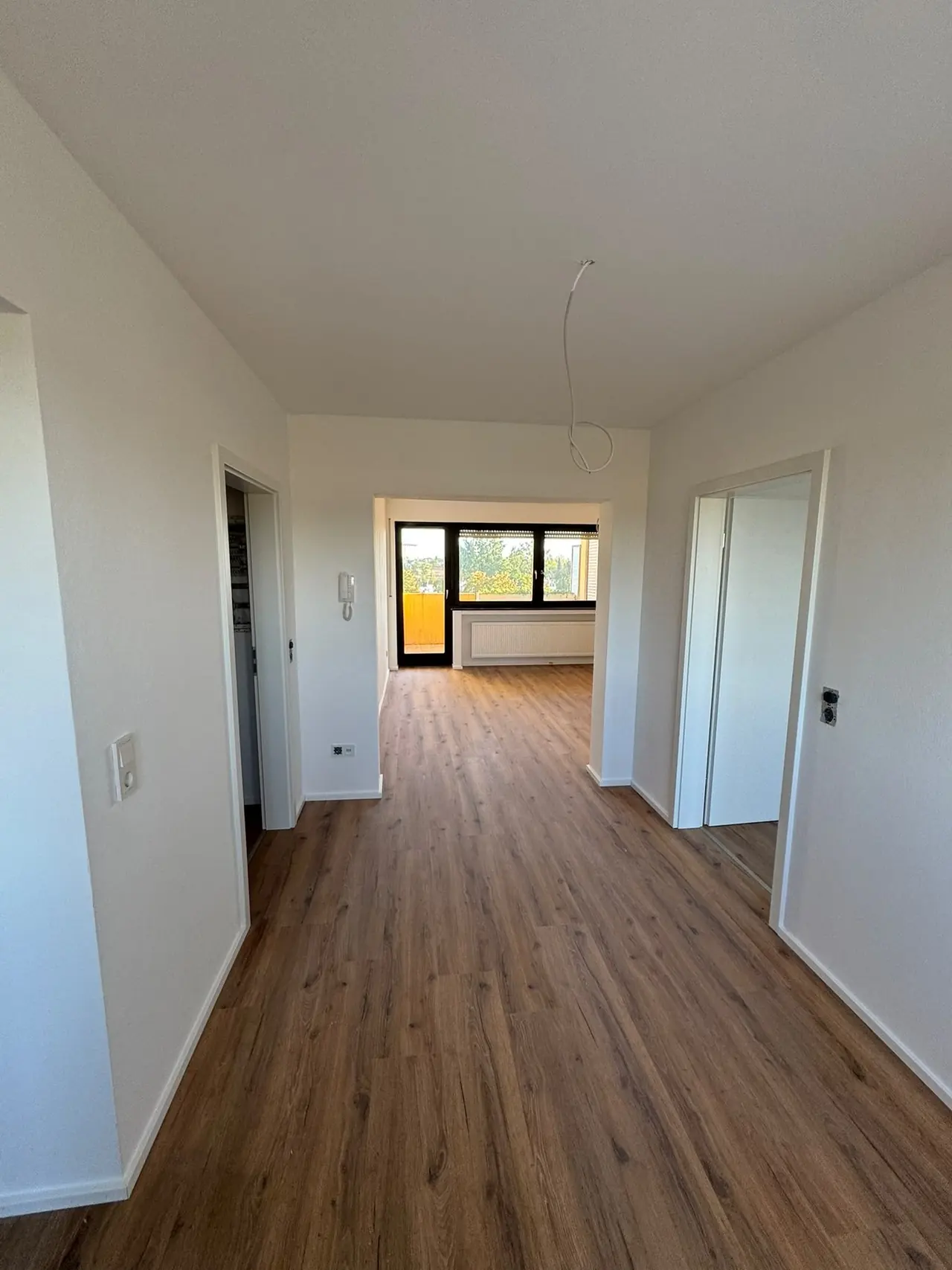 Straubing, Wohn- und Essbereich nach der Sanierung: Blick durch den hellen Flur in den Wohnraum mit Boden in Holzoptik