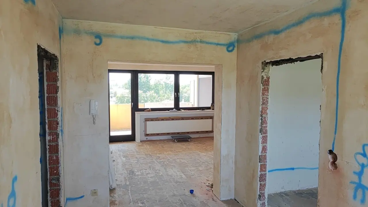 Straubing, Wohn- und Essbereich vor der Sanierung: offene Wanddurchbrüche und unverputzte Wände mit blau markierten Leitungswegen